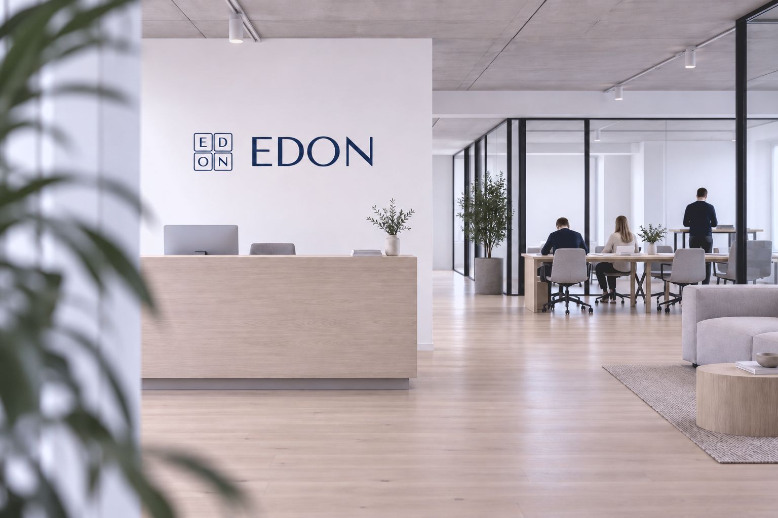 The EDON logo on the wall of a bright reception area, with three people working at a long table in the open office beyond