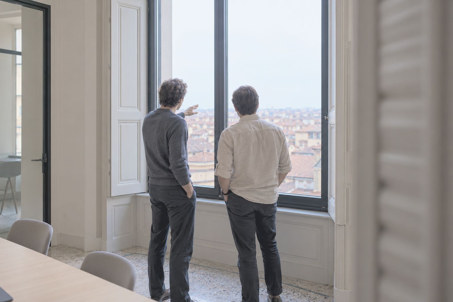 Two colleagues at a tall window looking out over the city